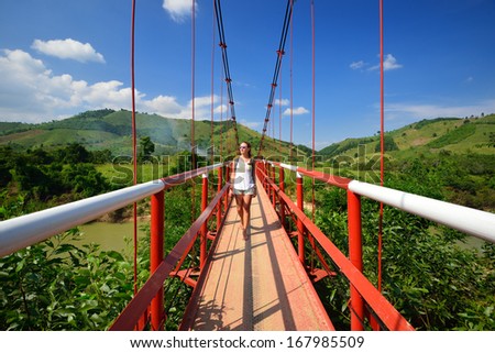 Traveler passes the river on a suspension bridge on the background of green mountains. Vietnam