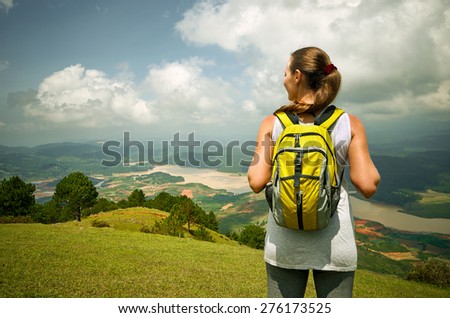 Portrait of happy traveler woman with backpack standing on top of the mountain and enjoying valley view