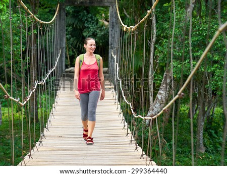 Hiking woman - hiker walking on bridge in forest.  Traveller. Woman hiking smiling happy on bridge with backpack during summer outdoors.