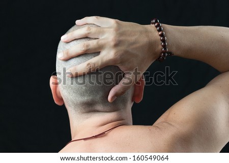 Close-up of a buddhist man wearing a mala feeling his newly shaved head, shirtless and shot from behind.