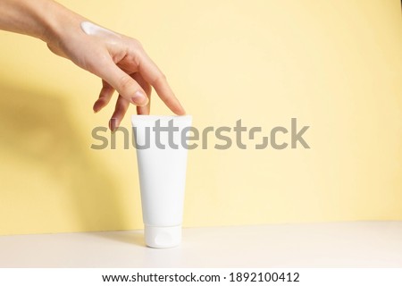 
female hand with applied cream touches cosmetic tube on beige background. Concept of cream, hand lotion. Winter skin care. Copy space