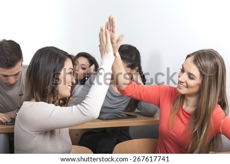Two female students clap their hand together while other students are bored