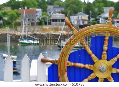Boat Wheel on a blue fence with boats in the background