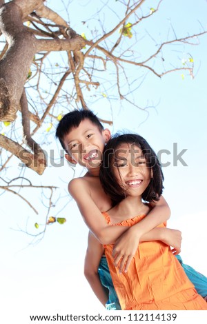 Portrait of a happy little girl carrying her brother in beautiful bright sunny day