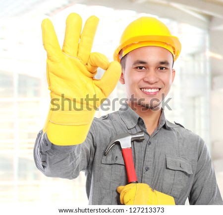 Portrait of young worker with tool belt giving you thumbs up