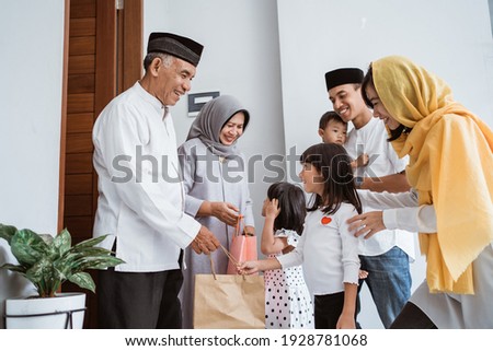 happy asian family giving present to their muslim grandparents during eid mubarak celebration. suprise gift to family