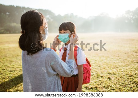 mother help her daughter to put on the mask before going to school in the morning
