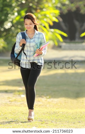 Portrait of beautiful young woman with bag and books walking in campus park