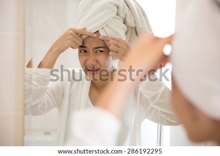 A portrait of an asian woman pressing acne on her forehead