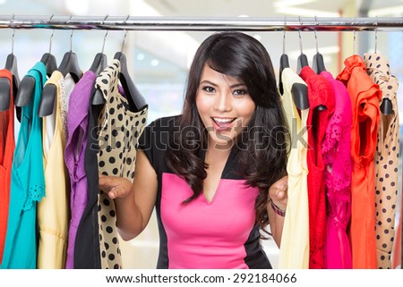 A portrait of a beautiful woman posing on the rack of clothes in a shop