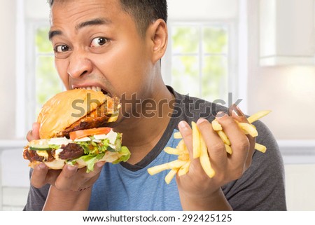 A portrait of a young man bite his big burger deliciously while the other hand holding chips