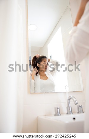 A portrait of a Beautiful asian woman tying her hair while smile at the mirror