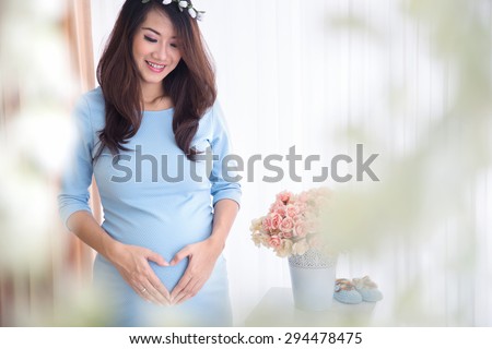 A portrait of a pregnant asian woman touching her big belly happily, heart shape hand gesture