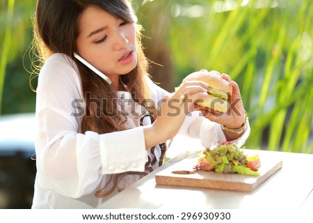 portrait of multitasking woman talking on the phone while eating burger