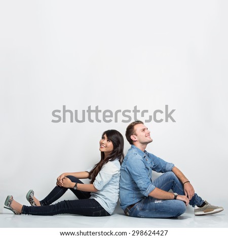 A portrait of a mixed couple thinking looking up and sitting back to back on the floor