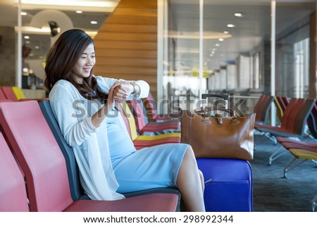 Woman in the airport lounge sitting in chair by the window looking at her watch waiting for her schedule to fly