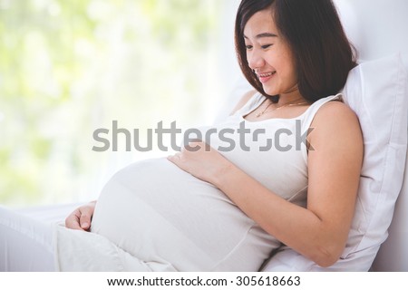 A portrait of a beautiful pregnant woman smiling looking at her belly while lying on the bed