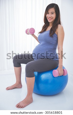 A portrait of a beautiful asian pregnant woman doing exercise with swiss ball, smiling