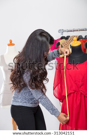A portrait of a young fashion designer or Tailor working on a design or draft, she takes measure on a dressmakers dummy
