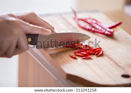 Hand slicing Chili pepper with Knife on chopping board on wooden background.