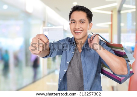 A portrait of a young asian man holding shopping bags and credit card, close up