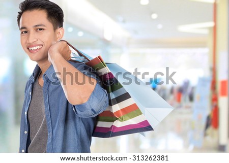 A portrait of a young asian man holding shopping bags, close up
