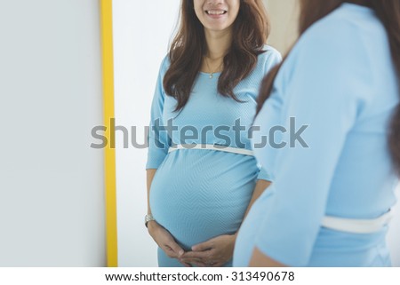 close up portrait of pregnant woman belly posing infront of a mirror, smiling happily