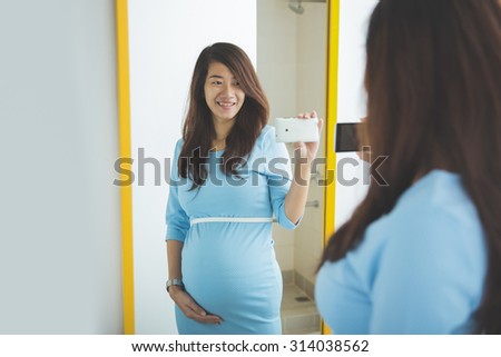 A portrait of Asian pregnant woman taking picture of her self in the mirror