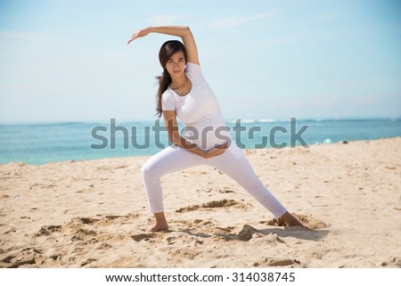 A portrait of a pregnant asian woman doing yoga in the sea shore