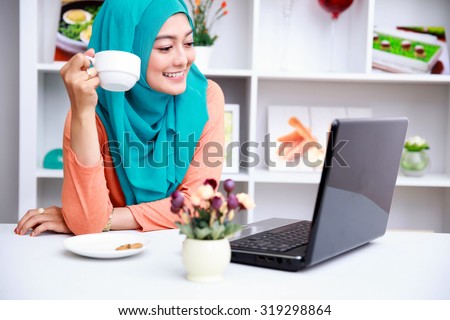 portrait of young muslim woman enjoying morning day with a cup of tea and movies on laptop
