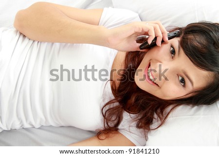 Beautiful young asian woman talking on the phone while lying in the bed.