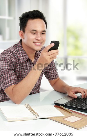 young man using a laptop and texting on mobile phone in his house
