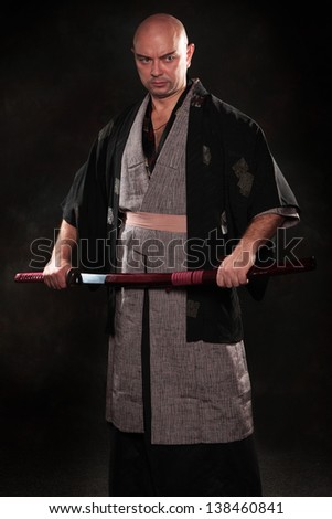 The man in the image of a samurai  covered in kimono with sword in hand  on dark background