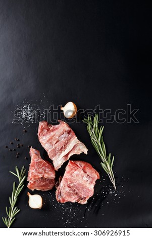 slices of frozen meat with rosemare and onion on black paper