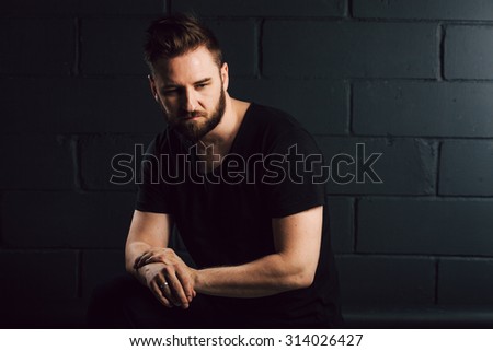 handsome bearded men in black shirt thinking about his life near brick wall