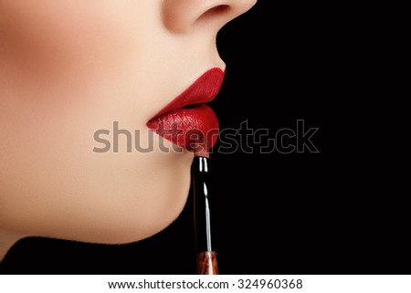 closeup macro photo of brush with lipstick and natural great red lips of young woman on black background