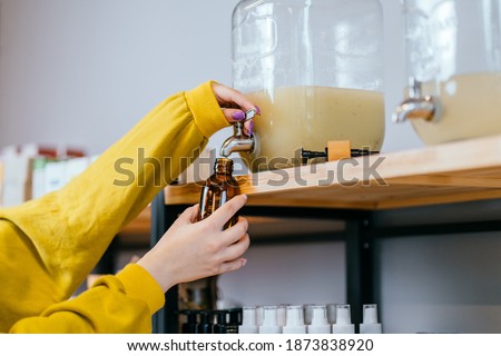 Unrecognizable woman pouring shampoo from a dispenser. Containers with natural biodegradable household chemicals in zero waste plastic free store. Dispensers for detergents, shampoo, soap, conditioner