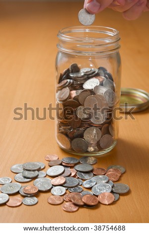 Putting coins in jar, counting spare change on the desktop