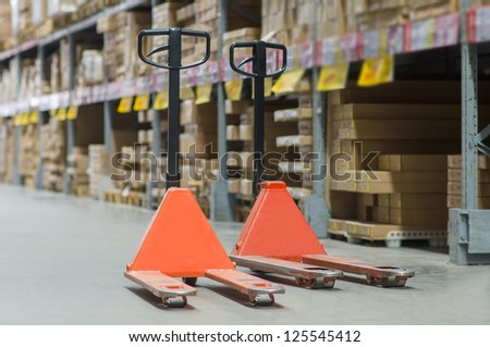Rows of shelves with huge cardboard boxes and orange storage carts on floor in modern warehouse