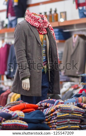 Mannequin in winter coat and sweaters on table in front of it in store