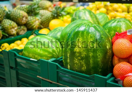 Huge watermelons, grapefruits and pineapples on boxes in supermarket