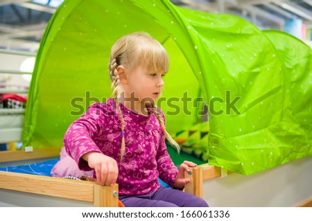 Adorable girl sit on loft bed in furniture shop