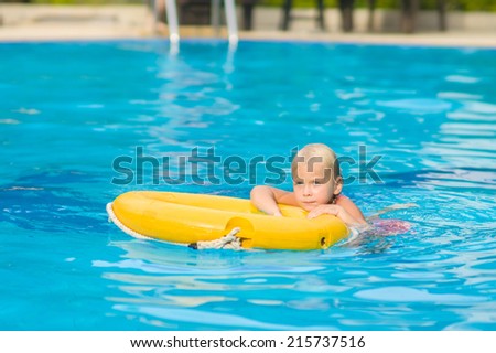 Adorable girl swim in pool with life ring in tropical beach resort