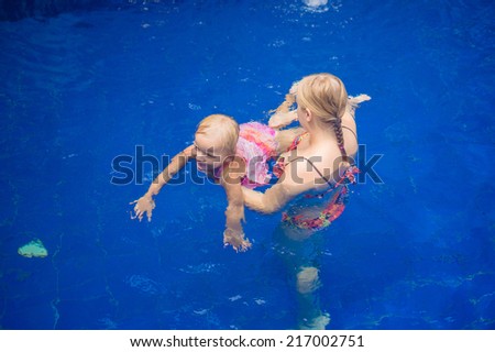 Young mother and adorable daughter having fun in pool. Learning daughter to  relax in water