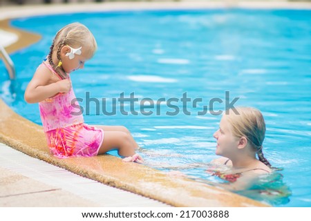Mother and daughter with flower behind ear have fun at pool side in tropical beach resort