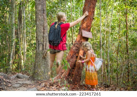 Mother and daughter touching tree with information poster at hiking trail to mountain top