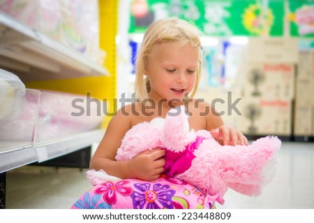 Adorable girl play with plush toy and pillow sitting on floor in department section