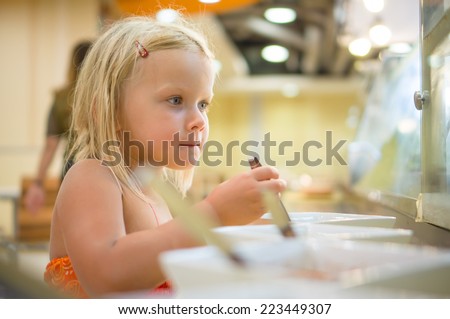 Adorable girl select dishes under shopping window on food court in mall
