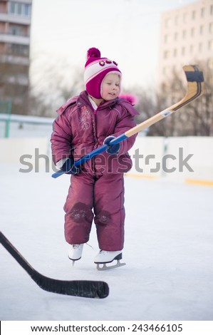 Adorable girl play with hockey stick in skates  on ice rink