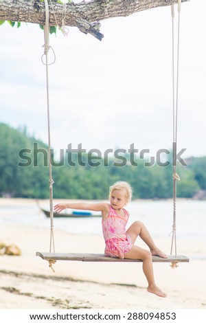 Adorable girl in pink swimming suit on swing on the beach